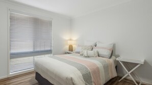 A bedroom with a bed, a bedside table with a lamp, and a window with blinds.
