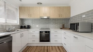 A modern kitchen with white cabinets, grey tiled backsplash, stainless steel appliances, and a wooden floor.