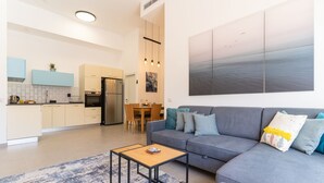 Un salon moderne avec un canapé gris, une table basse et, au fond, une vue sur la cuisine.