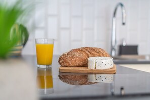 Een ontbijtpresentatie met een glas sinaasappelsap, een brood en een stukje kaas op een houten plank.