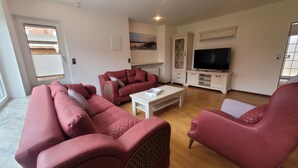 Una sala de estar con un sofá seccional, una mesa de centro, un televisor sobre un mueble bajo y un cuadro en la pared.