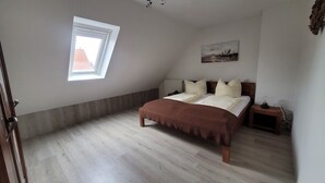 Un dormitorio con cama, mesita de noche, ventana y un cuadro en la pared.