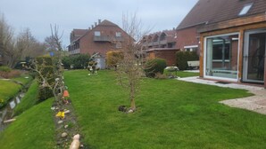 Un jardín residencial con césped, un árbol pequeño y una casa de ladrillo con puerta de vidrio.