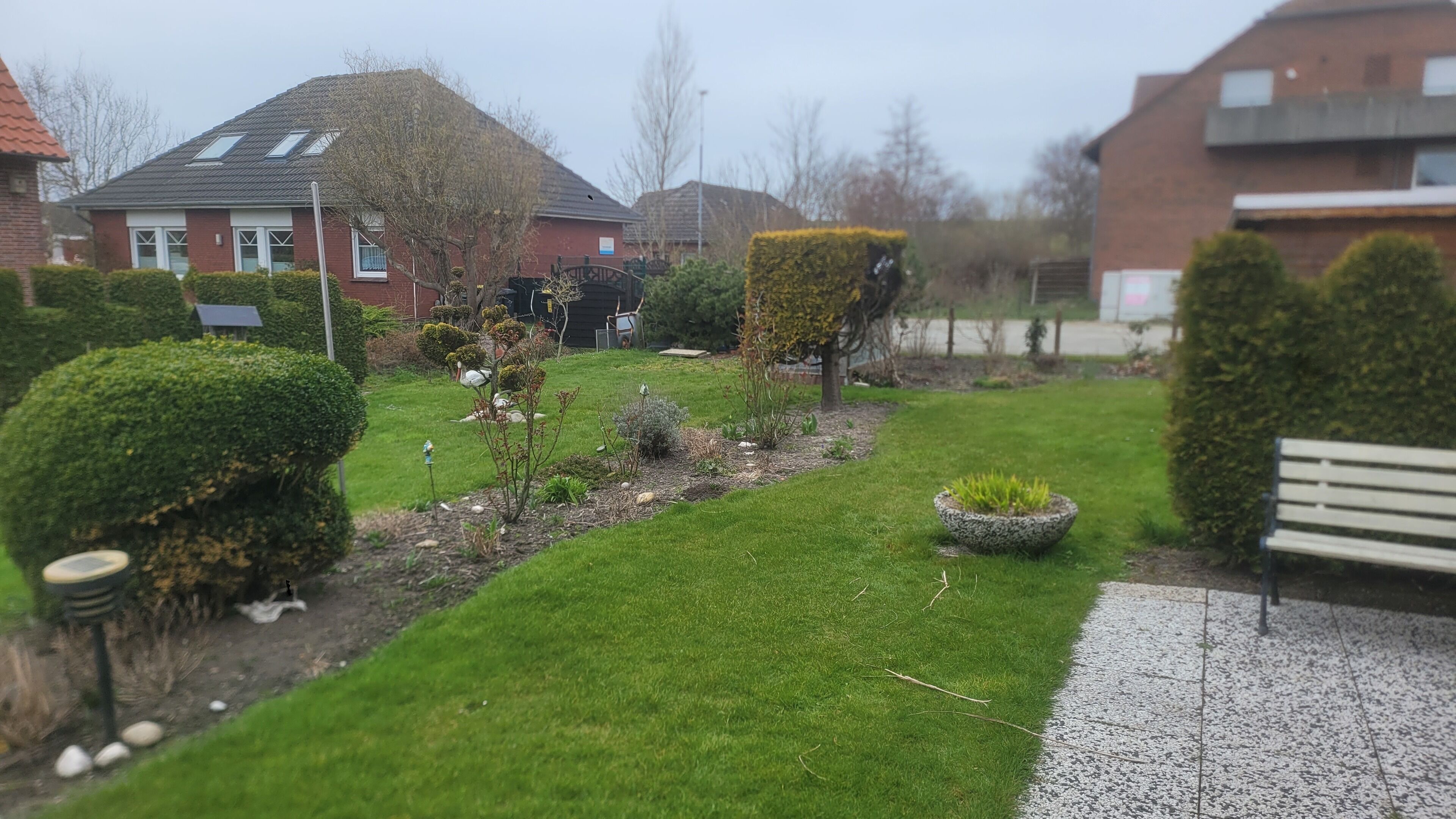 Jardim bem cuidado, com diversos arbustos e uma pequena área gramada.