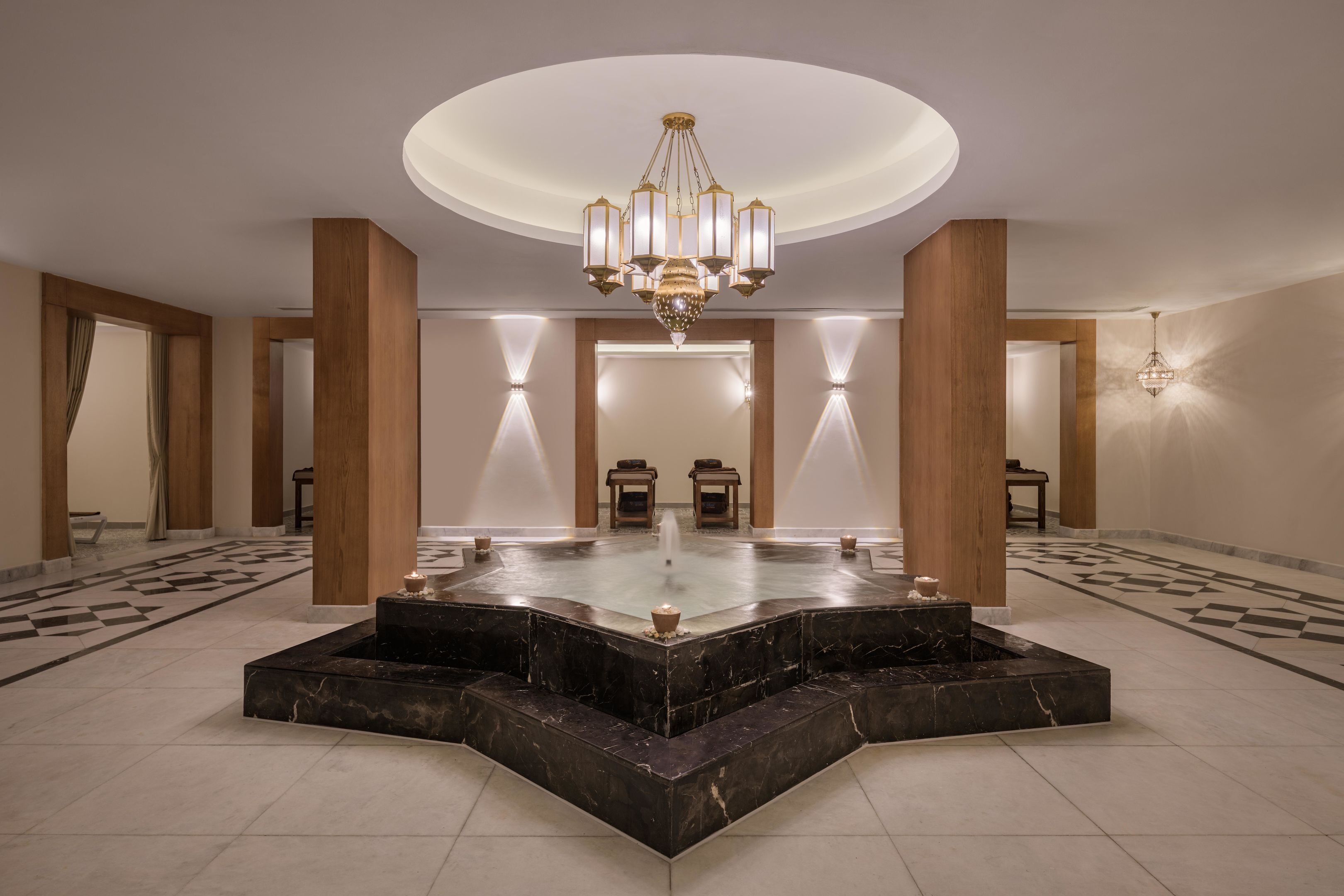 A spacious lobby with a central fountain, elegant lighting, and a checkered floor pattern.