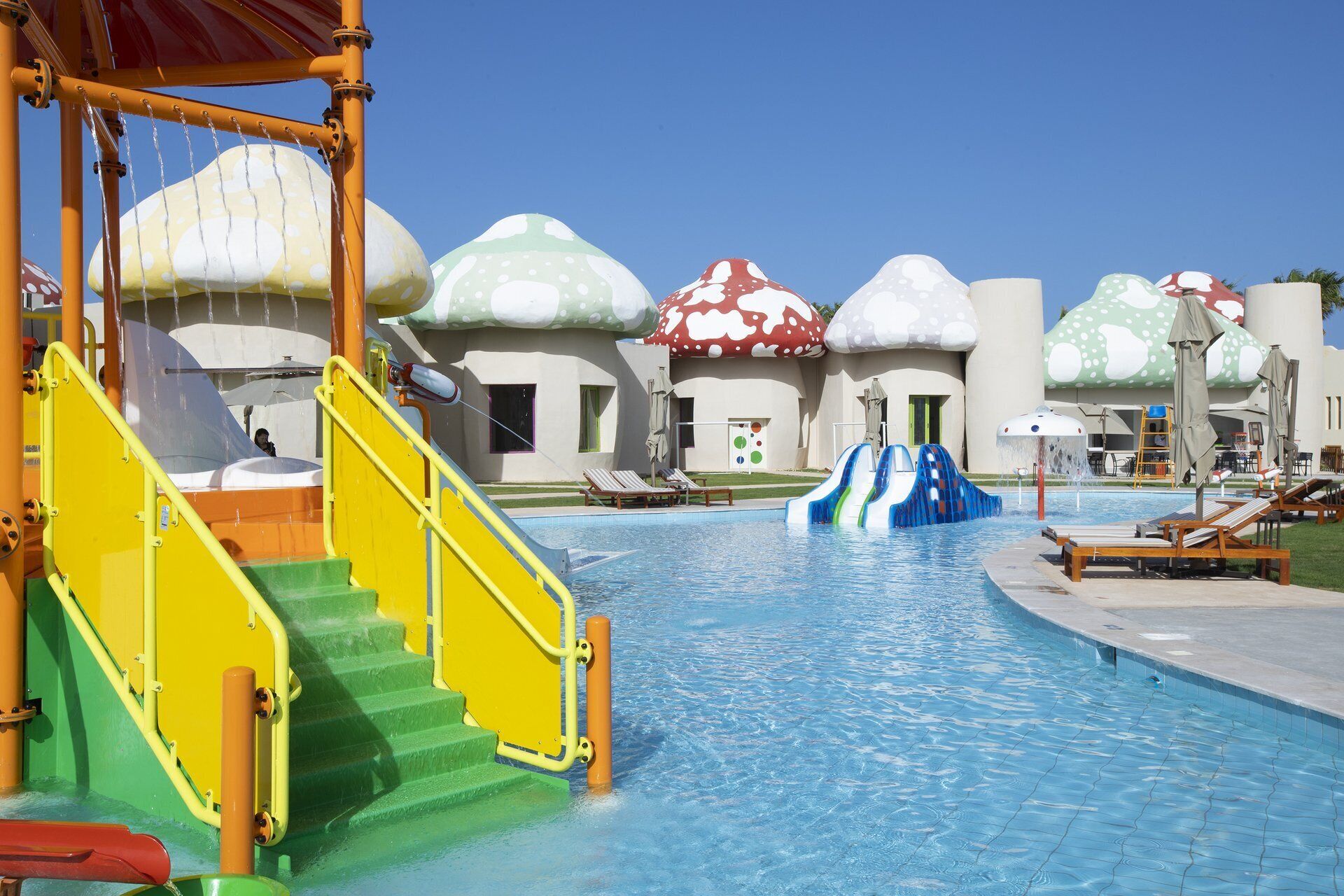 Uma área de piscina com escorregador, escadas e espreguiçadeiras.