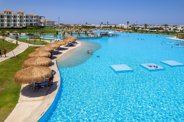 A large outdoor swimming pool with multiple lanes, surrounded by thatched umbrellas and lounge chairs.