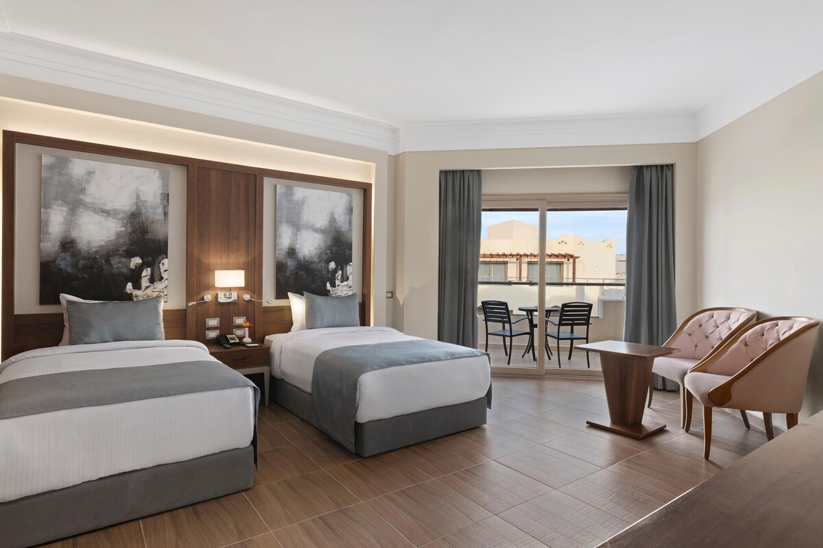 Habitación de hotel con dos camas, un escritorio, una silla y un balcón con vistas.