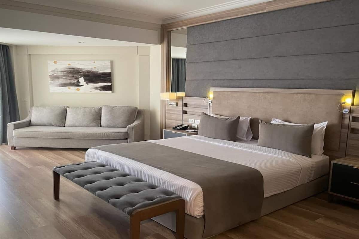A modern hotel room with a large bed, a sofa, a bench, and a nightstand.