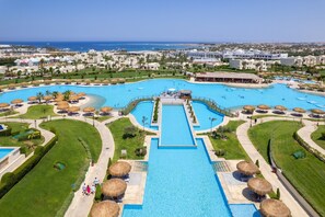 Vue aérienne d’un complexe hôtelier doté d’une piscine centrale, de plusieurs petites piscines et d’une zone de plage.