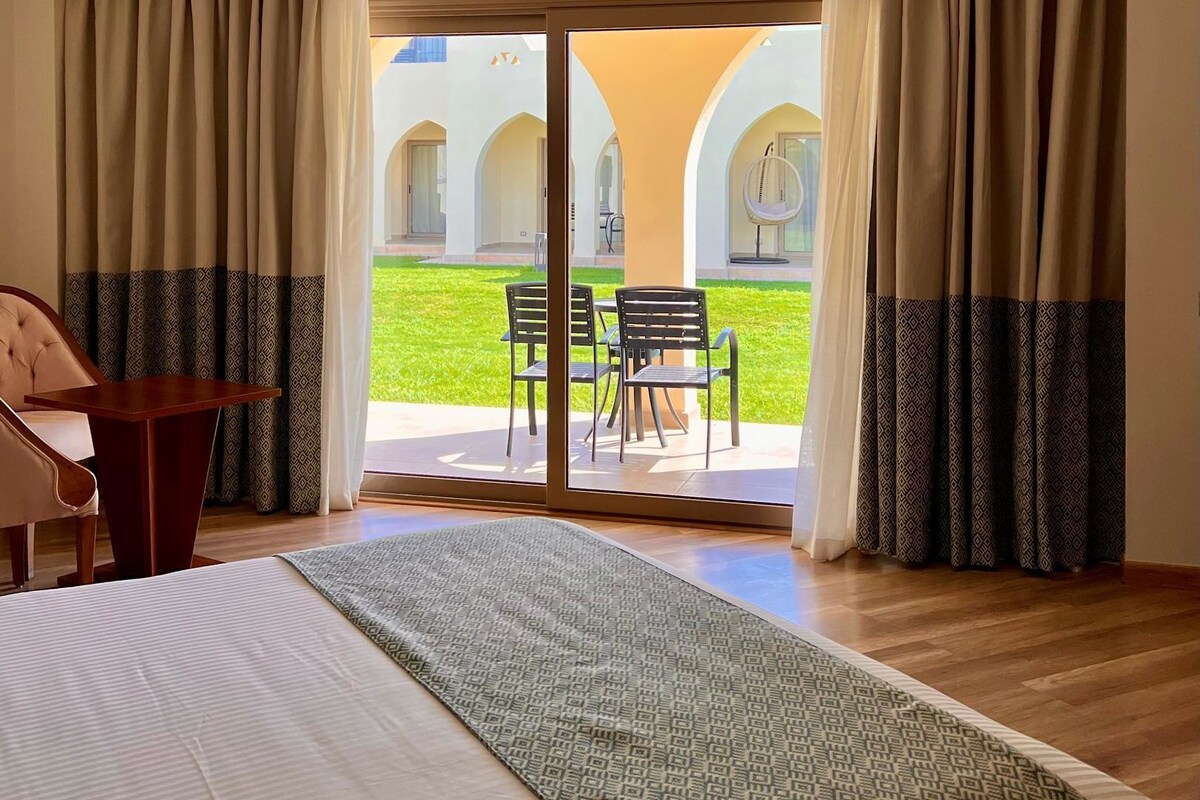 Una habitación de hotel con cama, escritorio y vistas a un patio exterior con sillas y una mesa.