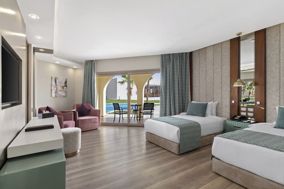 A hotel room with two beds, a desk, a TV, a chair, and a view of the pool.