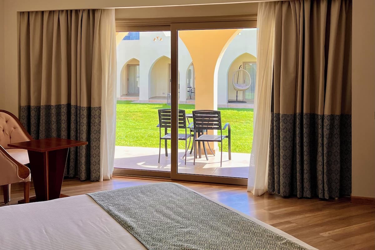 A hotel room with a bed, a desk, and a view of an outdoor patio with a table and chairs.