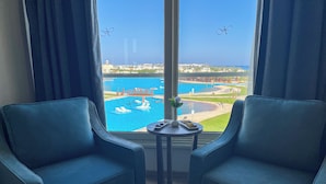 A room with two blue armchairs facing a large window overlooking a pool and a view of a cityscape. - Xanadu Makadi Bay - High Class All Inclusive (Makadi Bay)