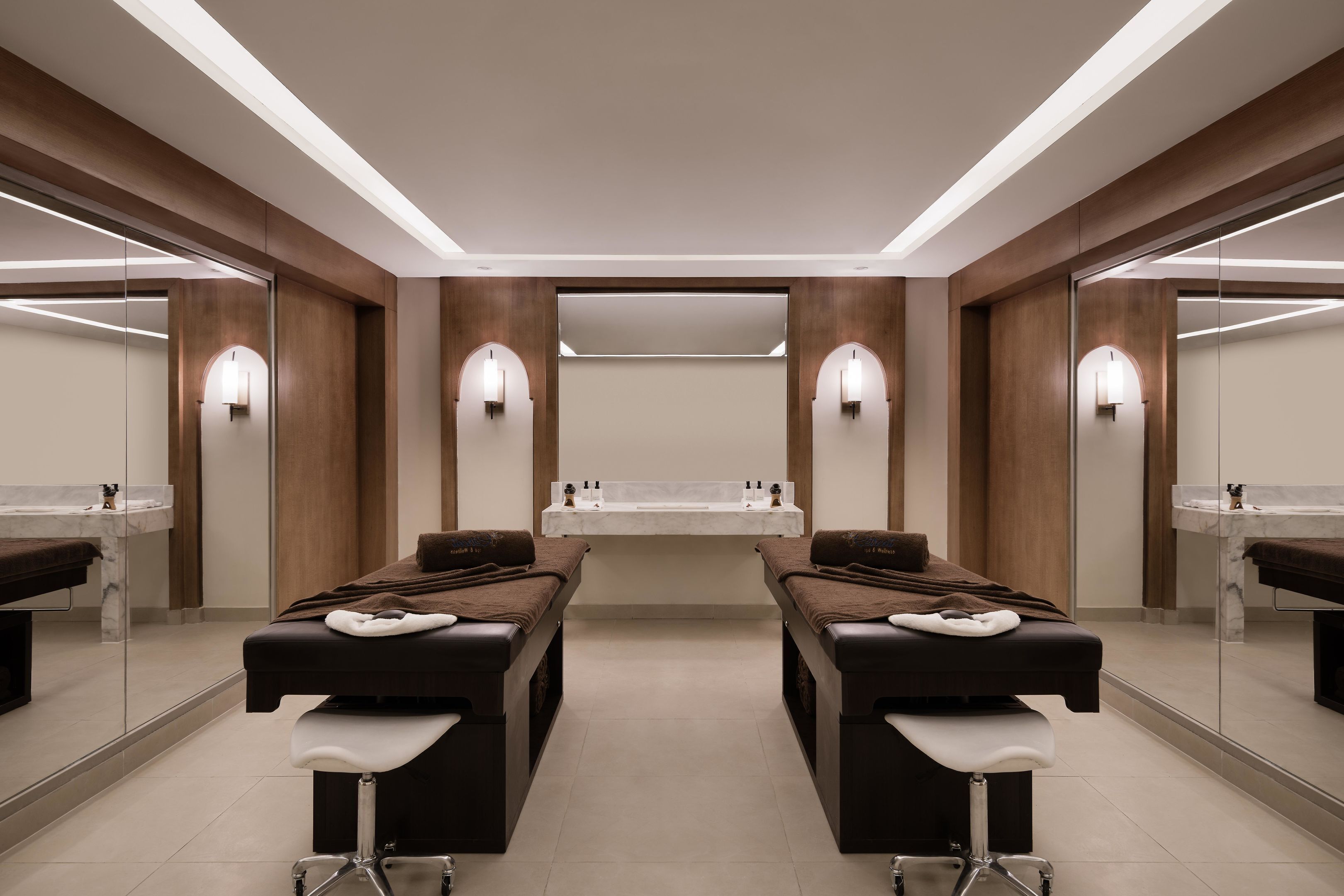 Un moderno spa con dos camillas de masaje, un lavabo central e iluminación empotrada.