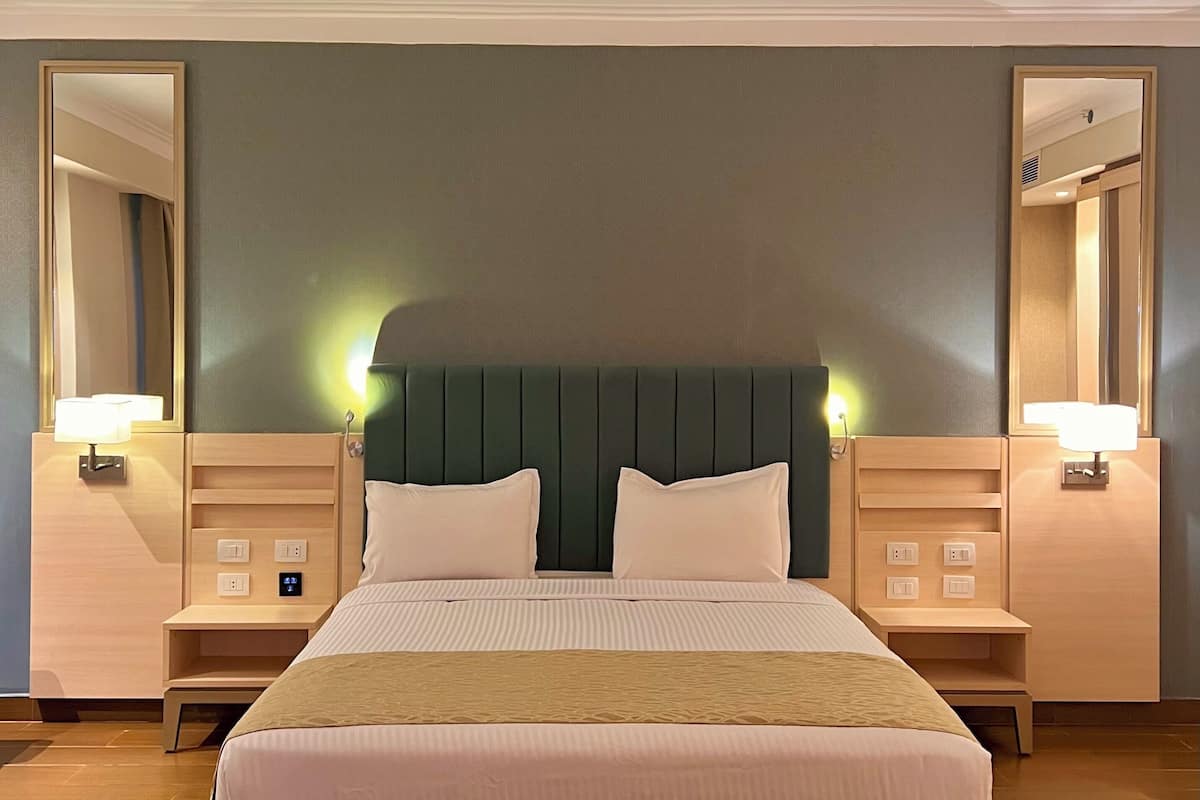 A hotel room with a large bed, bedside tables with lamps, a headboard, and a mirror on the wall.