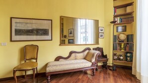 Une pièce avec un plancher en bois, un canapé, une chaise, une bibliothèque et un tableau encadré au mur.