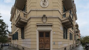 Un immeuble d’angle avec une grande porte en bois, un balcon et une plaque au-dessus de la porte.