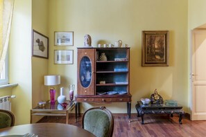 A room with a dining table, a cabinet with shelves, a chair, and framed pictures on the wall.