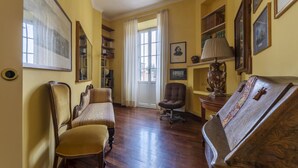 Une pièce avec un plancher en bois, un canapé, un fauteuil, un bureau avec une lampe et une bibliothèque.