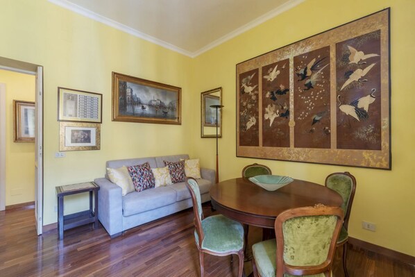 A dining area with a round table, four chairs, a sofa, and wall art.