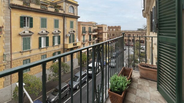 Un balcon donnant sur une rue, avec des plantes en pot et un immeuble à la façade jaune.