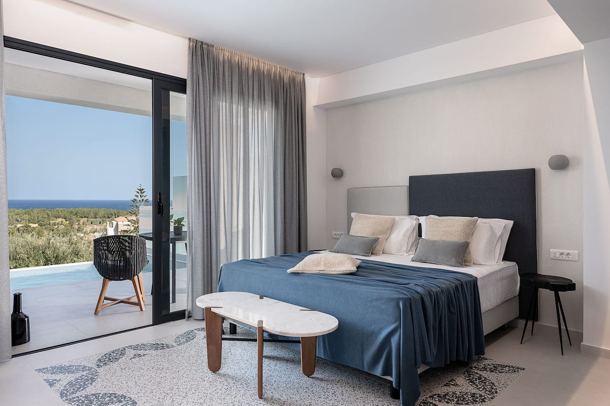 A modern bedroom with a large bed, a view of the sea, and a balcony with a chair.