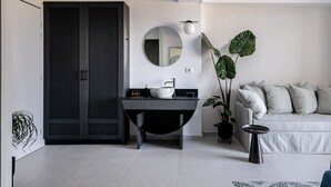 Une salle de bain moderne avec un miroir rond, un lavabo noir et une grande plante en pot.
