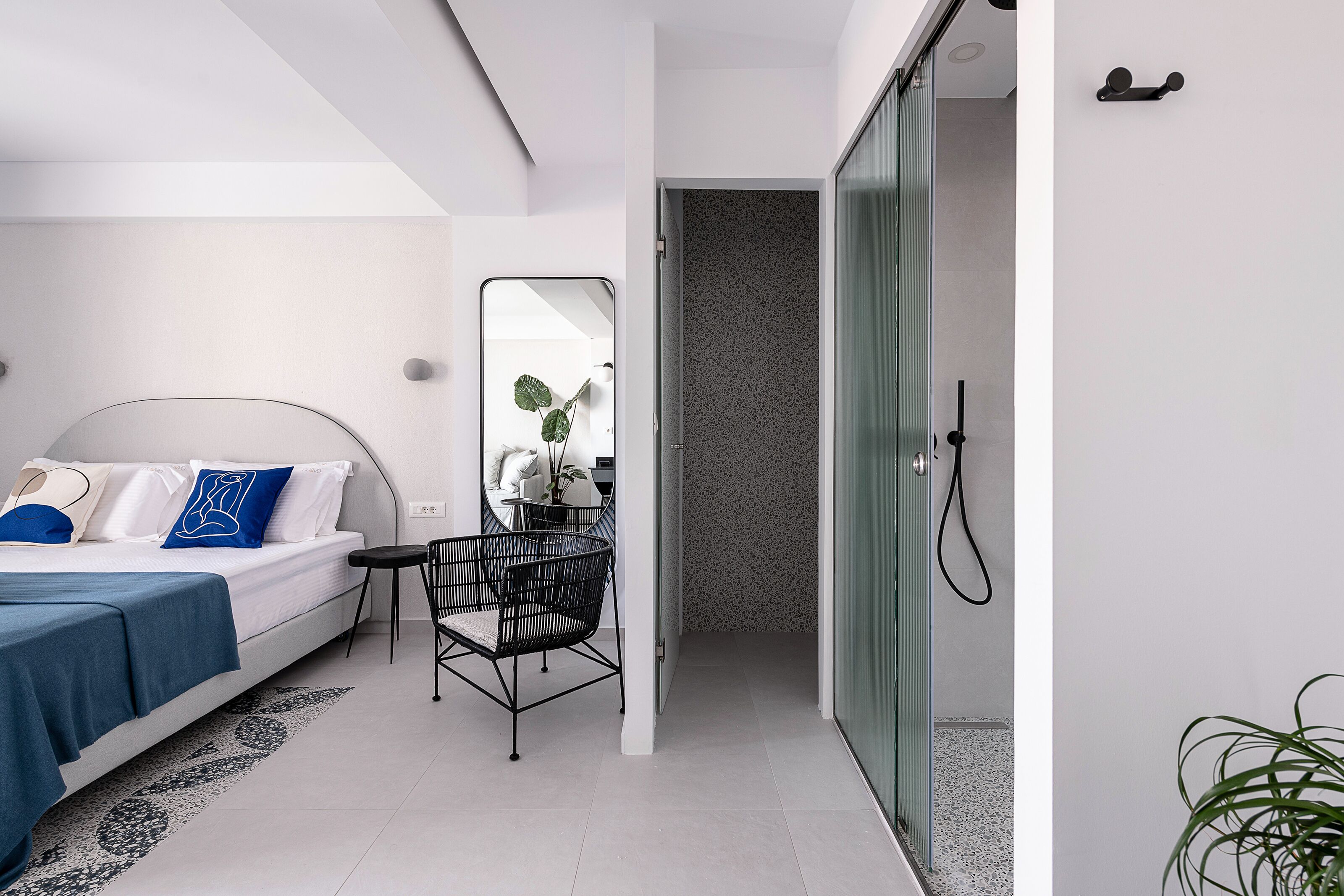 A modern bedroom with a bed, bedside table, chair, and a mirror.