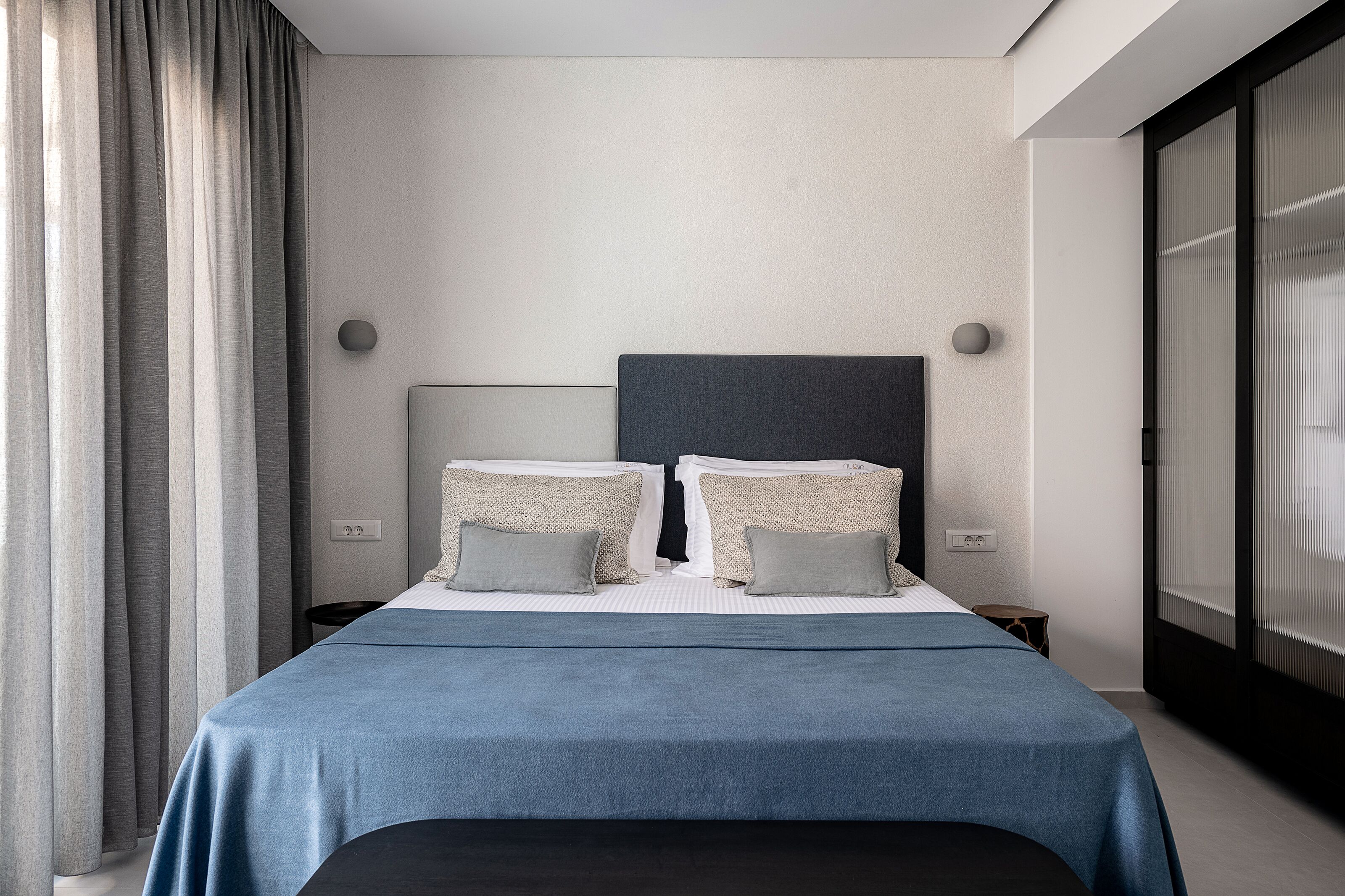 A modern hotel room with a bed, curtains, and a large window.