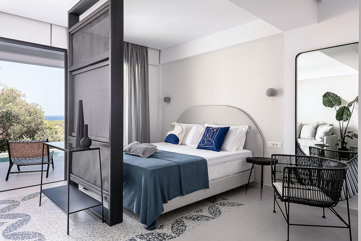 A modern bedroom with a large bed, a side table, a chair, and a mirror.