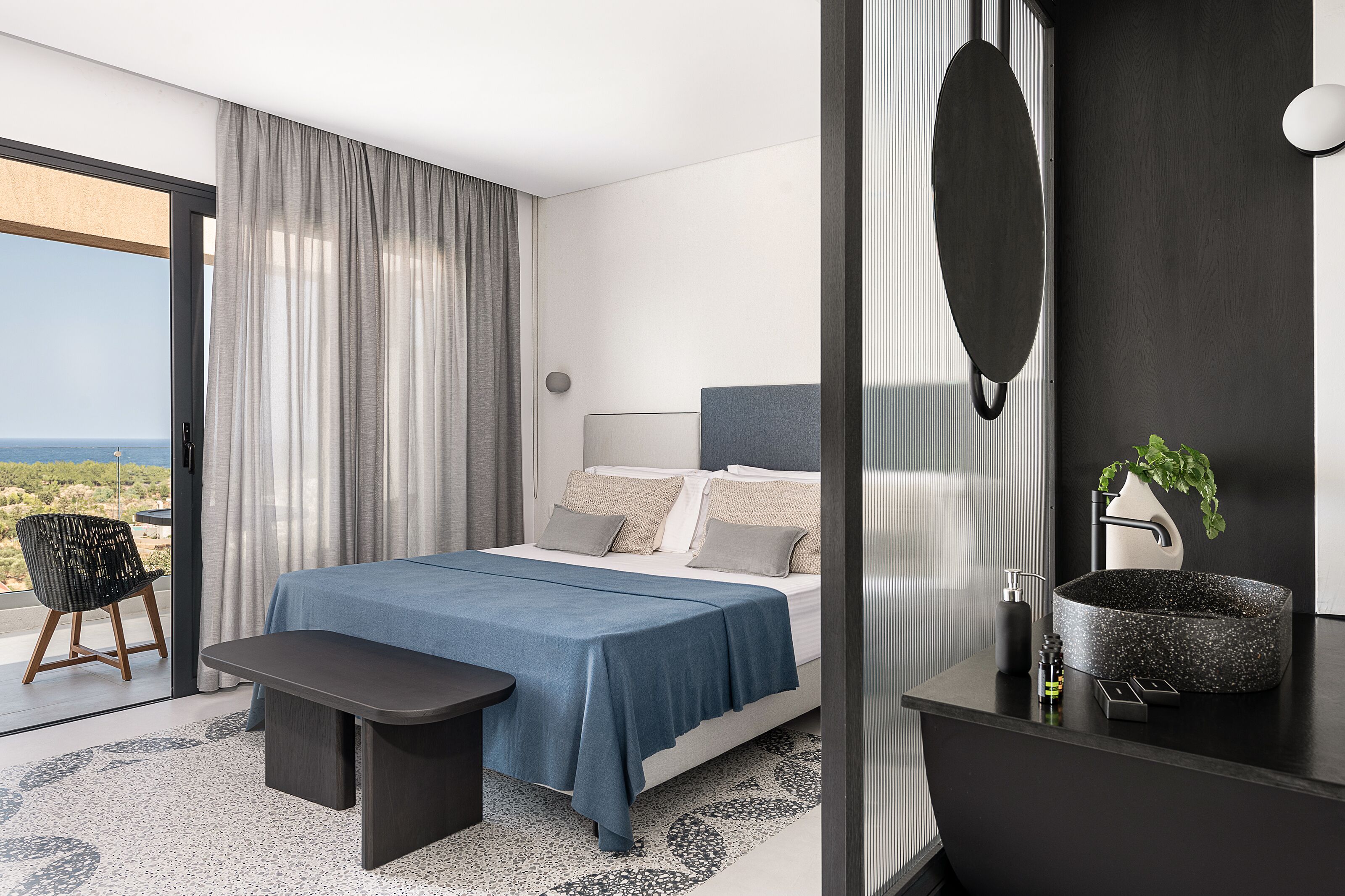 Et moderne hotelværelse med en seng, en bænk, et badeværelse med en rund vask og udsigt over landskabet.