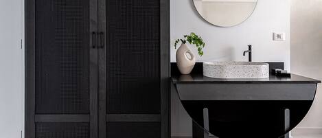 Un baño moderno con un armario de madera oscura, un espejo redondo y un lavamanos minimalista.