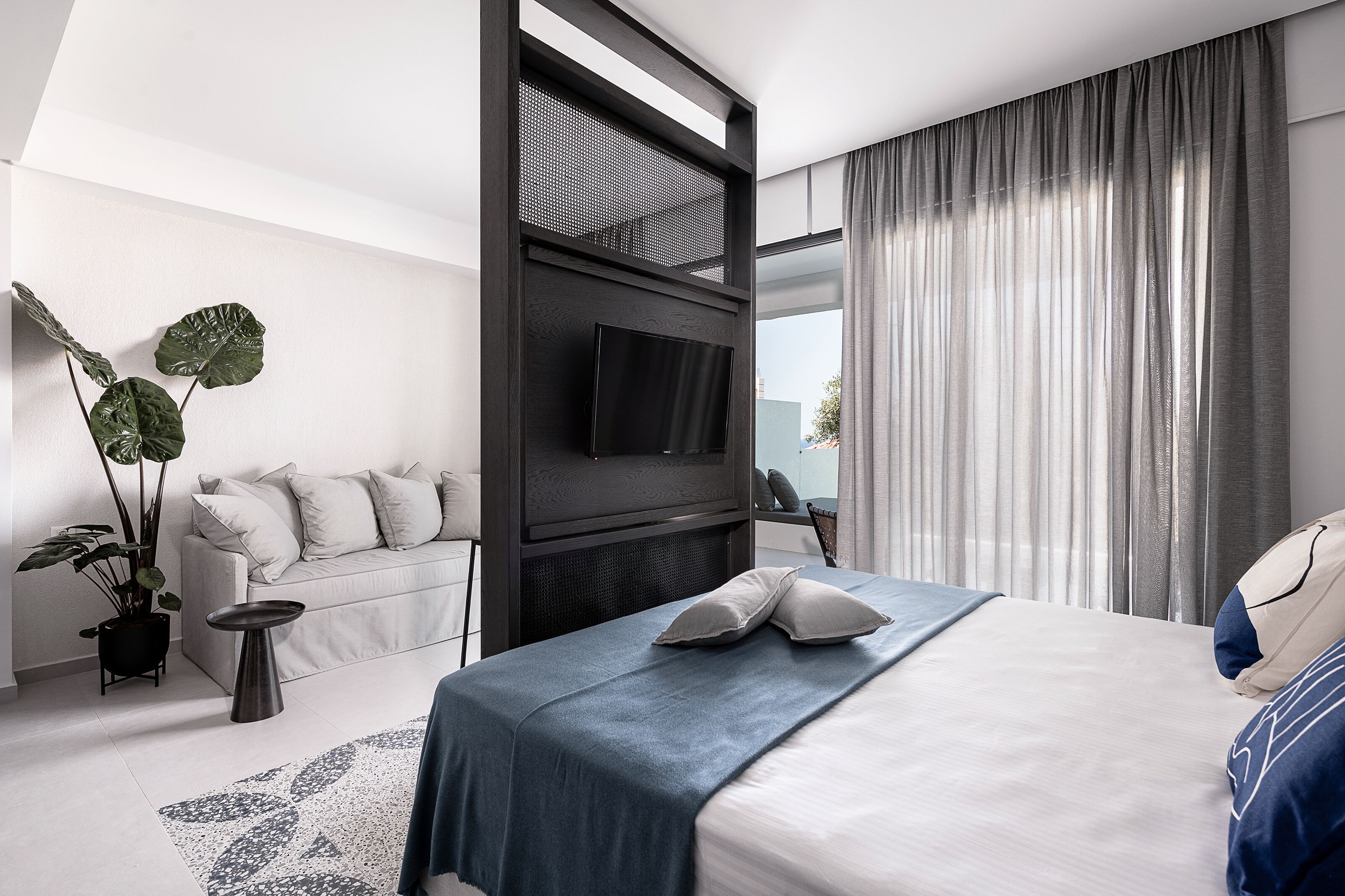 Une chambre d’hôtel moderne équipée d’un lit, d’un canapé, d’une télévision et d’une grande fenêtre avec des rideaux.
