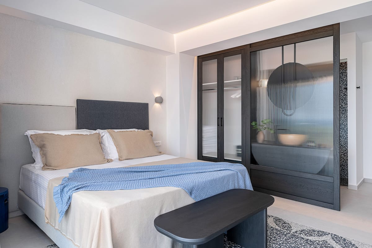A modern bedroom with a bed, bedside table, and a large sliding glass door leading to a bathroom.