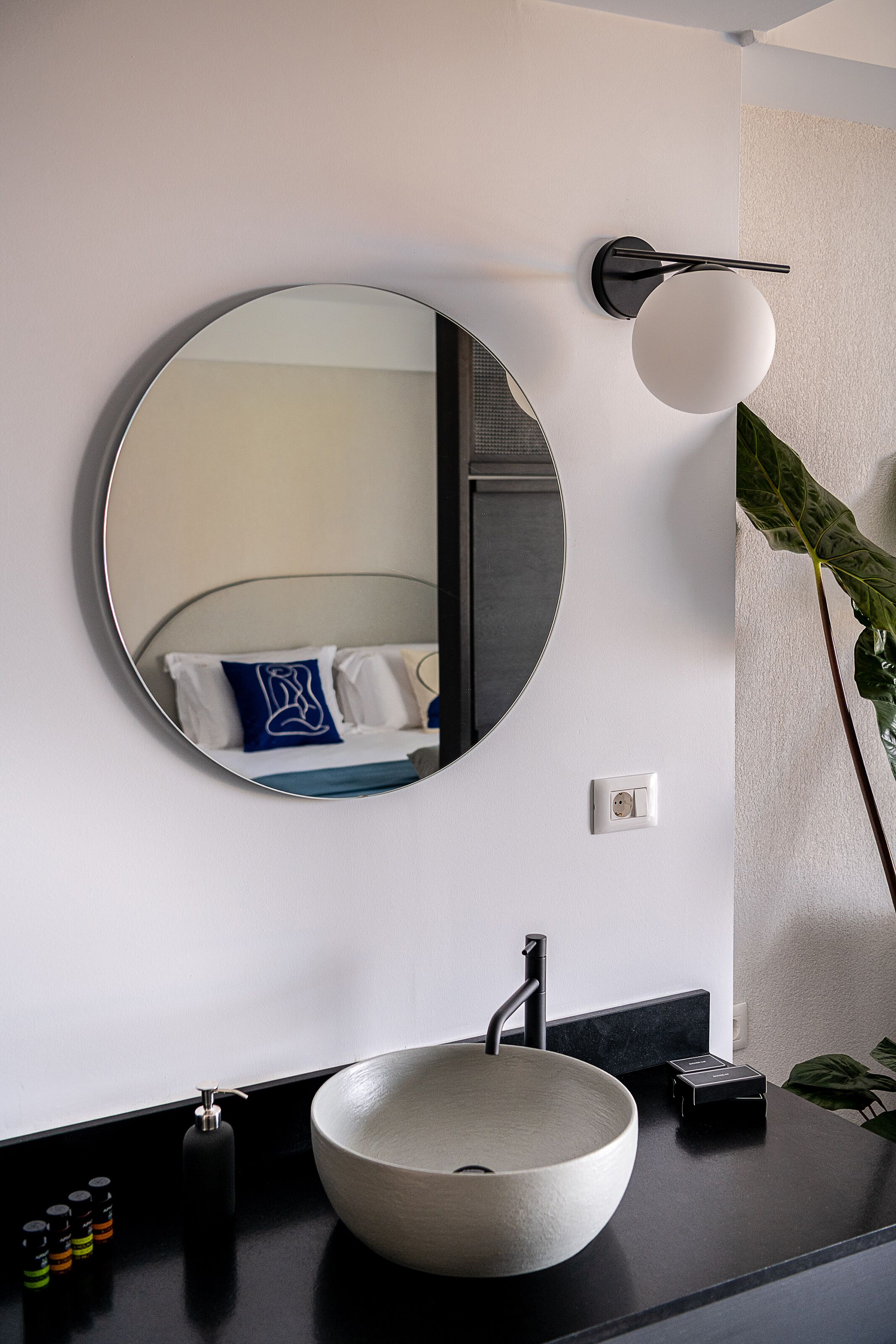 Une salle de bain moderne avec un miroir rond, un lavabo rond et un plan de toilette noir.