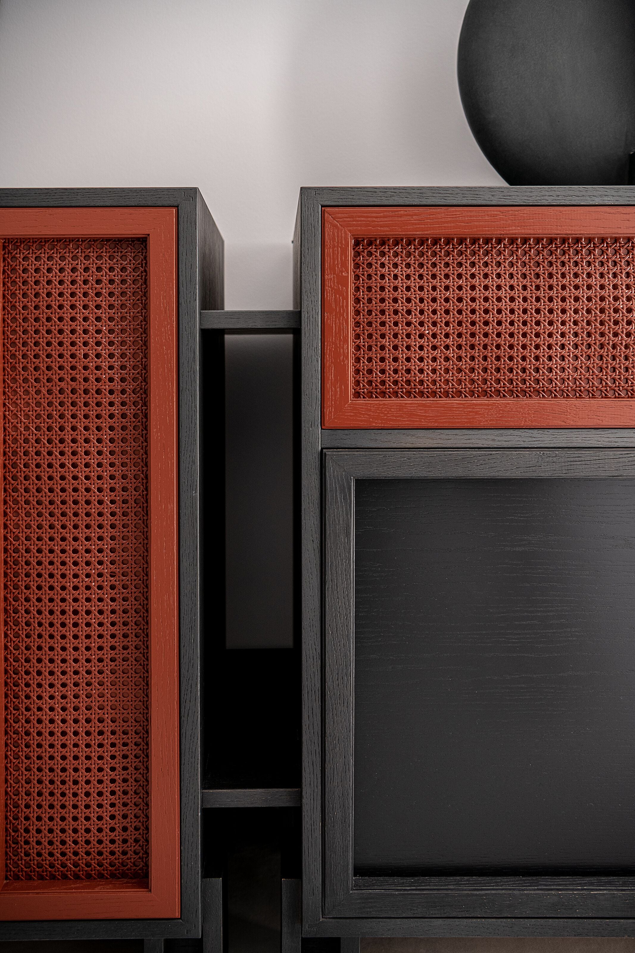 A modern, dark-colored furniture piece with a red accent panel and a perforated design.