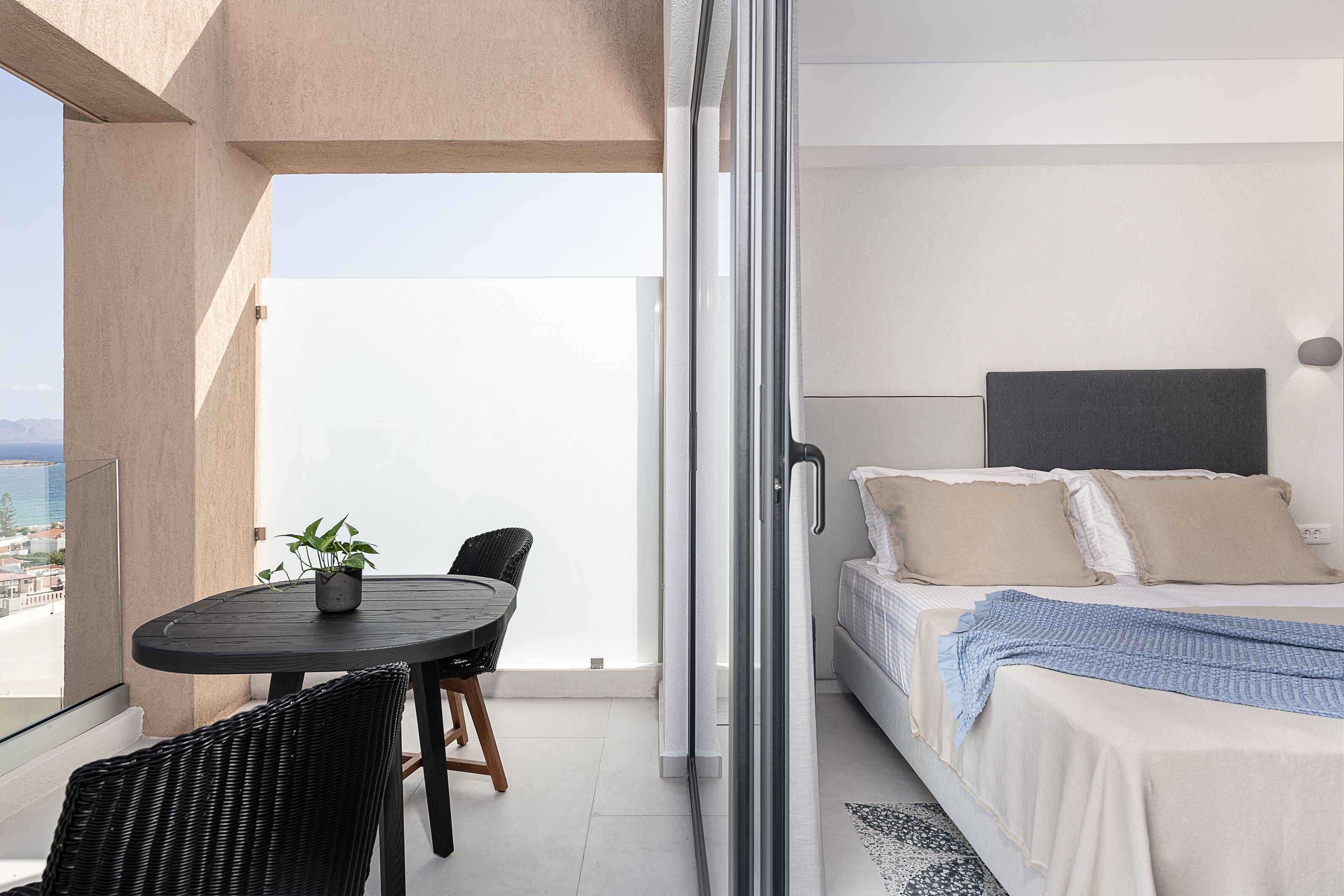 Un balcone con tavolo e sedie, un letto con cuscini e vista sulla città.