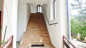 Uma escada leva a uma porta com um painel de vidro, tudo envolto por paredes brancas e uma pequena janela.