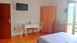 Quarto com cama, escrivaninha, cadeira, guarda-roupa e televisão presa na parede.