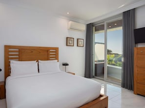 A modern bedroom with a wooden headboard, a large bed, a nightstand, a flat-screen TV, and a sliding glass door leading to a balcony.