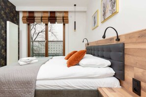 Hotelkamer met een groot bed, een houten hoofdeinde, een raam met uitzicht op gebouwen en een wandlamp.