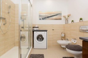 Een moderne badkamer met een douchecabine van glas, een wasmachine, een bidet en een toilet.