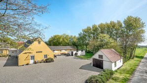 A yellow building with a gravel courtyard, a white building with a red roof, and surrounding greenery. - Pet friendly apartment in Strynø (Strynø)