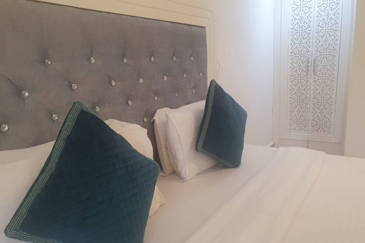 A bed with a tufted headboard, two pillows, and a window with a decorative screen.