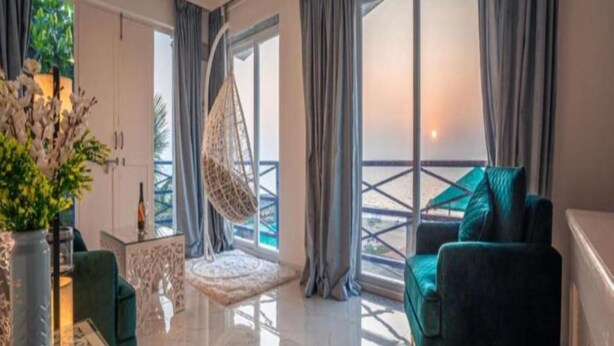 A modern living room with a sofa, a hanging chair, and a view of the outdoors through large windows. - Lillywoods Zac Beach Resort (Calangute)