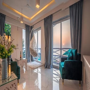 A modern living room with a sofa, a hanging chair, and a view of the outdoors through large windows. - Lillywoods Zac Beach Resort (Calangute)