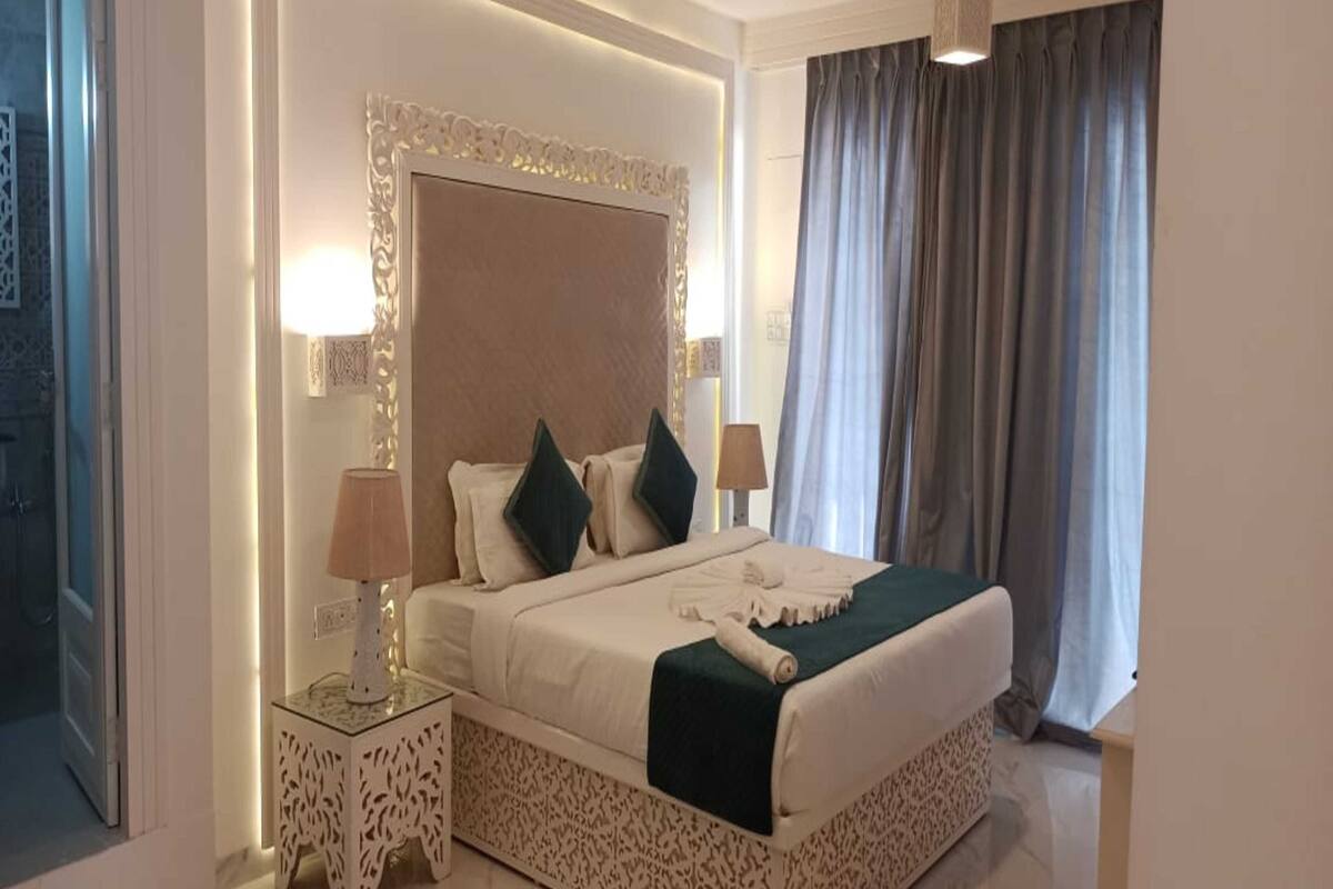 A hotel room with a large bed, two bedside tables, a headboard, and a window with curtains.