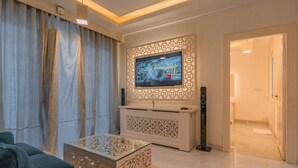 A modern living room with a flat-screen TV mounted on a decorative wall, a sofa, a coffee table, and a ceiling fan. - Lillywoods Zac Beach Resort (Calangute)