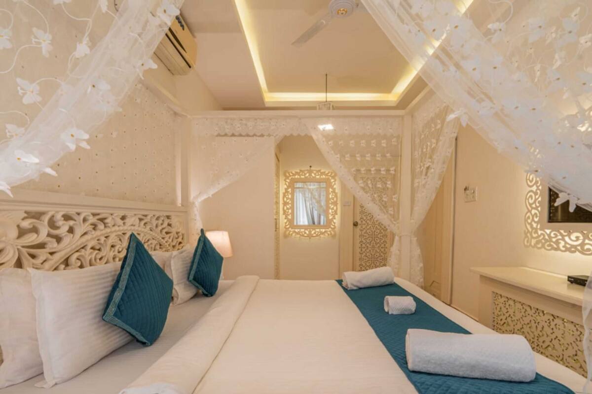 A hotel room with a large bed, decorative canopy, and ornate wall designs.